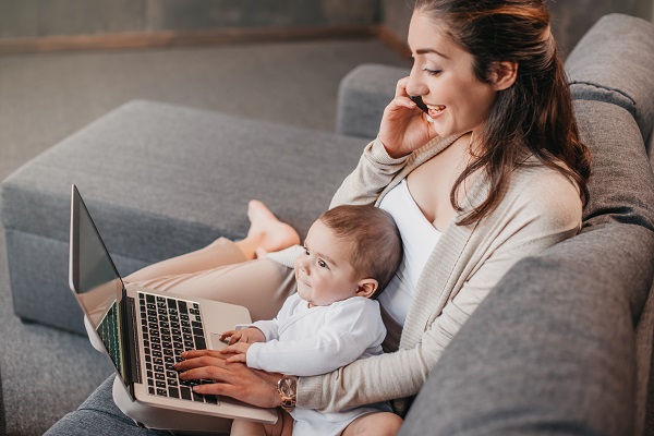 A business woman works from her home office while holding a happy baby.